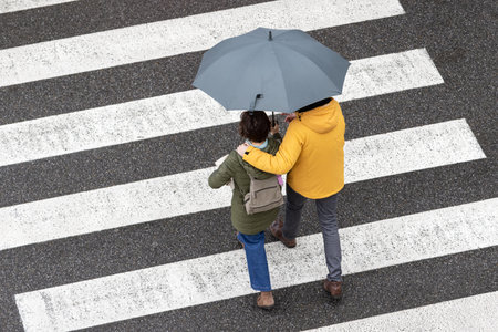 Scene of a couple walking together with an umbrella on a city zebra crossing on a rainy dayの写真素材
