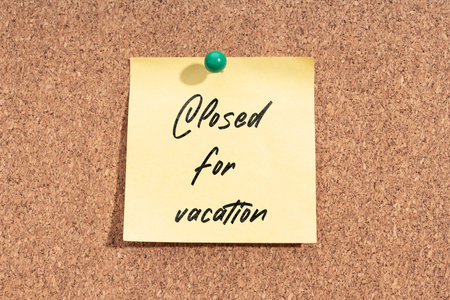 Yellow sticky note with message Closed for Vacation on cork board