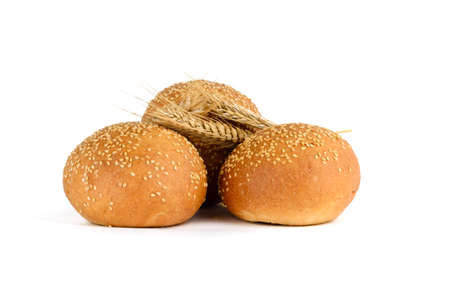 Three fresh buns with sesame seeds and three ears of wheat on a white backgroundの写真素材