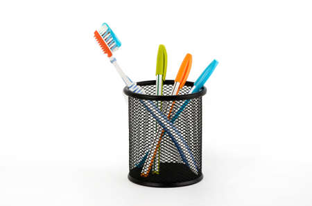 Toothbrush and three pens in a basket on a white backgroundの写真素材