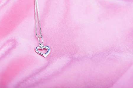A small, silver heart on pink satinの写真素材
