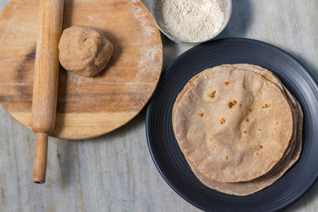 Top view of a stack of tortillas with a rolling pin and flour on a wooden table.