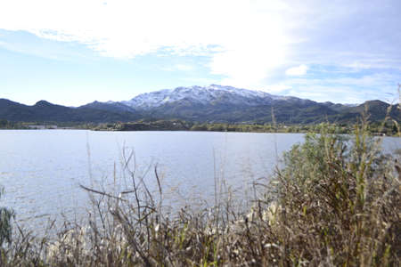 Lake with vegetation around on a sunny day, snowy mountains in the background.の写真素材