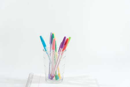 pens of different colors in a glass glass over a blank notebookの写真素材