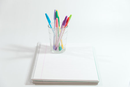 pens of different colors in a glass glass over a blank notebookの写真素材