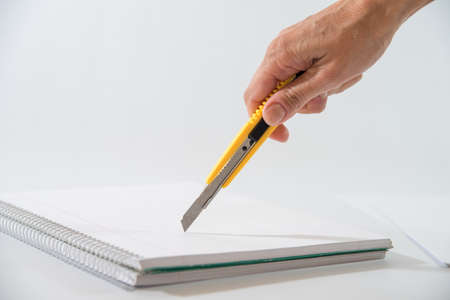 hand with a cutter in hand cutting the sheet of a notebookの写真素材