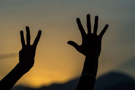 person making silhouettes with their hands in the darkness of a sunsetの写真素材