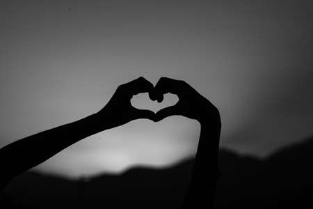 person making silhouettes with their hands in the darkness of a sunsetの写真素材