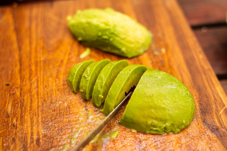Avocado peeled and sliced on top of a wooden tableの写真素材