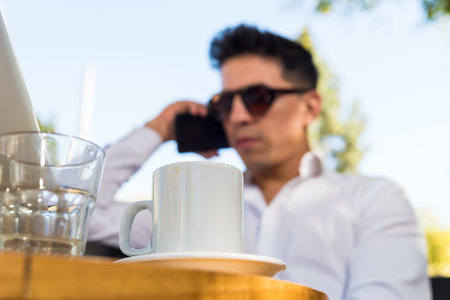 Man with glasses sitting outdoors talking on the phone, laptop and coffee on tableの写真素材