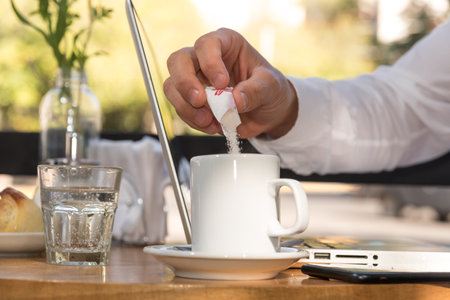 person putting sugar in their coffee, laptop on the tableの写真素材