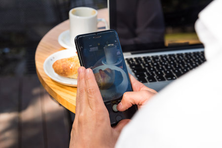 Sitting man taking pictures with his smartphone of the coffee he is drinkingの写真素材