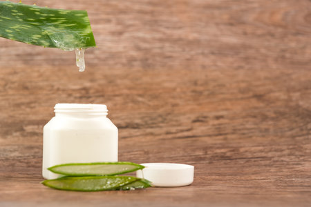 cut Aloe Vera leaf by draining into a plastic container on a wooden tableの写真素材