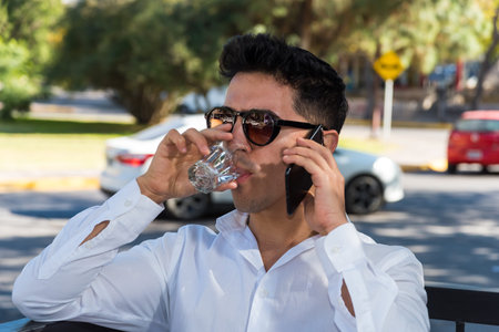 Man with glasses drinking sparkling water while holding his phone