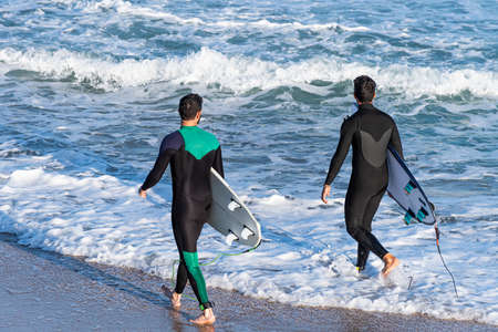 Back view of two young men with surfboardsの写真素材