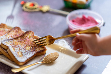 A kid hand sticks a fork in the traditional french toast with cinnamon on a gray background....