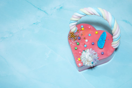 Pink heart shape cake on a blue marble background with a lot of small colorful candies . Valentine...
