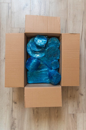 Glassware wrapped with blue wrapping nylon at the bottom of a cardboard box. Glassware wrapped in a...