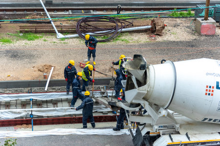 Tel Aviv, Israel - May 20 2021: Construction Workers working in the rain. Light rail tracks. blue collar worker. Concept Collaboration teamwork. Trucks, concrete mixer, bulldozerのeditorial素材
