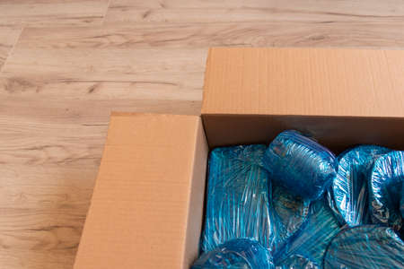 Glassware wrapped with blue wrapping nylon at the bottom of a cardboard box. Glassware wrapped in a box. Top view. Flat lay. Copy spaceの写真素材