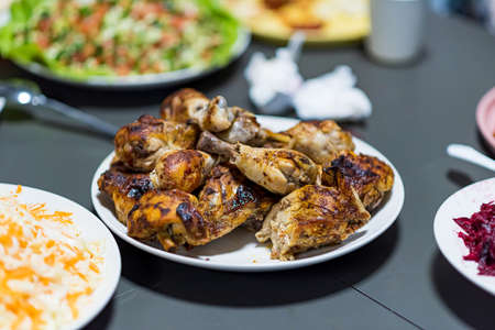 Chicken shanks, chicken legs are served on a plate with various salad plates in the backgroundの写真素材