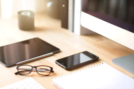 Close up of working place in office with wooden table and laptop laying ,Place of work. comfortable working place with laptop espresso smart phone notepad paper pen eyeglasses mouse laying on itの写真素材