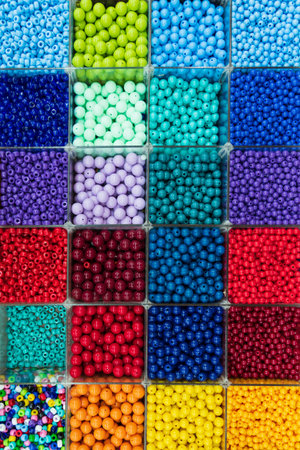 Beads are arranged and sorted by color. Background of colorful bright beads in boxes, set for...