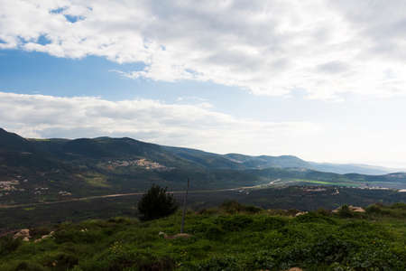 A view of a mountain range and a green valley in the morning at sunrise, against a dramatic back of blue skies and clouds. High quality photo. Travel concept hiking. North District Israelの写真素材