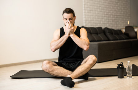 Sick man with runny nose sitting on black yoga mat. Stay home concept. Brunette young man blows his nose after workout. Practicing sports at home if you feel sick.の写真素材