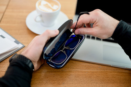 Take care of your eyeglasses. End of shift at remote work. Young man hides glasses in case. Male...