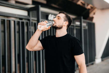 Man drinking water from plastic bottle after jogging with closed eyes. Hard workout. Take care of youself concept. Drink more water. Sport in big city concept.の写真素材