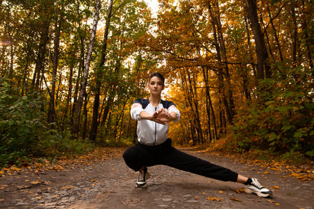 Athletic woman warms up in park before jogging. Healthy lifestyle concept. Sporty woman with hair in ponytail stretching her body and doing side lunge exercises. Female trail runner.の写真素材