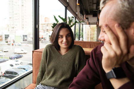 Blurred man on front listening crazy and funny stories of her girlfriend. Attractive woman in green sweatshort narrating something interesting to her boyfriend. Restaurant or cafe on background.の写真素材