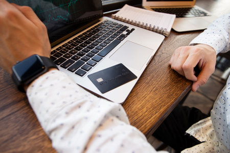 Black credit card lies on gray laptop. Cut view of young man. Dont enter your credit card details on suspicious sites. Man using credit card to make an online purchase. Financial literacy concept.の写真素材
