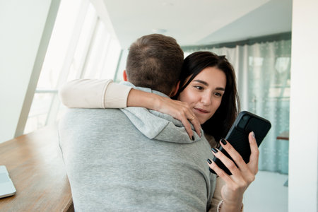 Woman texting other men when embracing her boyfriend. Lies will always pop up concept. Man trusts his wife but she deceives him. Cheating concept. Woman looking in her smartphone while hugging man.の写真素材
