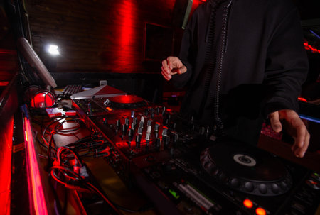 DJ hands on equipment deck and mixer at party. Cut shot of disk jockey in black hoody mixing music in night club. Night life concept. Hanging out with friends.の写真素材
