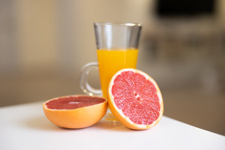 Organic food. Glass of citrus juice and cut halves of grapefruit on white table. Blurred yellow background. Healthy lifestyle. Vegan. Tasty breakfast. Take care of yourselfの写真素材