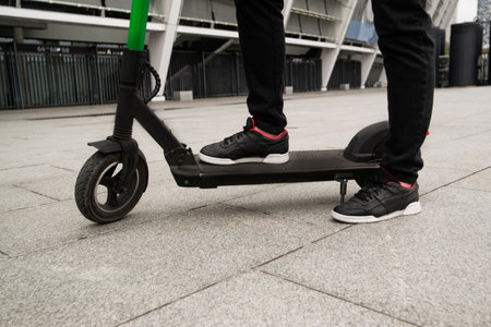 Cut view of male legs standing on e-scooter. Smart way to drive around a big city. Black stylish sneakers. Guy rented an electric scooter by smartphone application. Eco habits.の写真素材