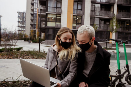 Young happy couple spending good time on bench near apartment blocks. They watch movies and laugh....