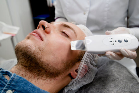 Cosmetologist is cleaning the young mans face from acne and scars by ultrasonicsの写真素材