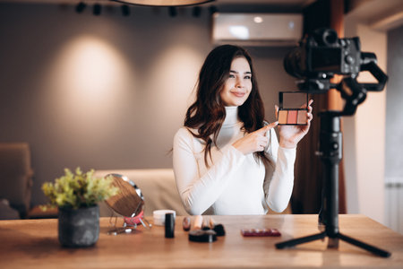Beauty blogger nice female filming daily make-up routine tutorial on camera. Influencer young woman live streaming cosmetics product review in home studio. Vlogger job. Showing makeup productsの写真素材