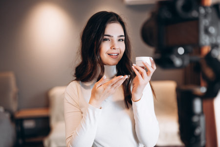 Pretty beauty woman promoting face cream. Famous blogger. Cheerful female vlogger is showing cosmetics products while recording video and giving advices for her beauty blogの写真素材