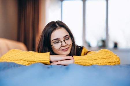 Nice girl wearing glasses and cute sweater is relaxing at home while working stying. Photo about young freelancer woman os working indoor. Student is studying online at home .の写真素材