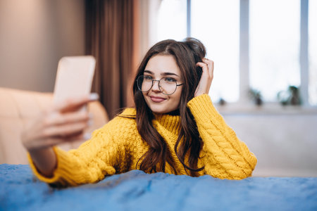 Nice girl wearing glasses and cute sweater is taking selfie. Photo about young freelancer woman os working indoor. Student is studying online at home .の写真素材