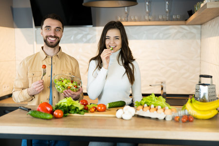 Young and beautiful vegetarian couple are smiling in the kitchen while cooking. Also they look happy and healthy because of using only nutrition and fresh food.の写真素材