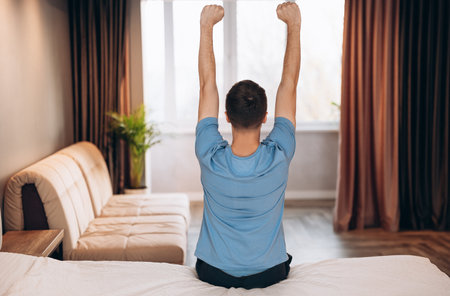 Good morning Young man waking up in bed and stretching his arms, back view, copy spaceの写真素材