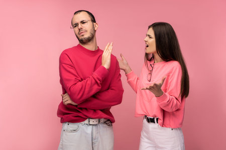 Photo of couple argues and looks unhappy together, isolated over pink background