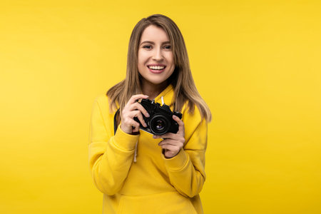Photo of attractive lady holds camera with smile and wants to make a photo. Wears casual yellow...