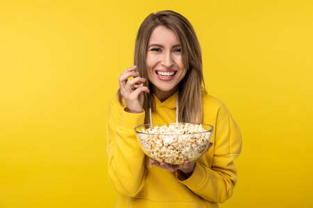 Photo of attractive lady holds plate of popcorn, with smile. Wears casual yellow hoody, isolated yellow color backgroundの写真素材