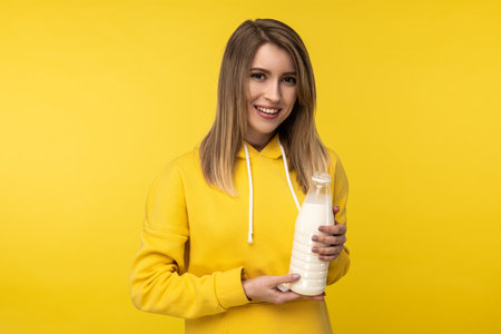 Photo of attractive lady holds bootle of milk, feels nice about dairy products. Wears casual yellow hoody, isolated yellow color backgroundの写真素材